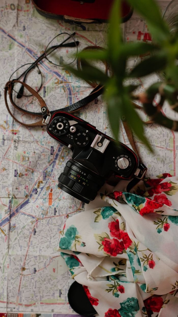 Flat lay of vintage camera on map with floral scarf, evoking travel and nostalgia.