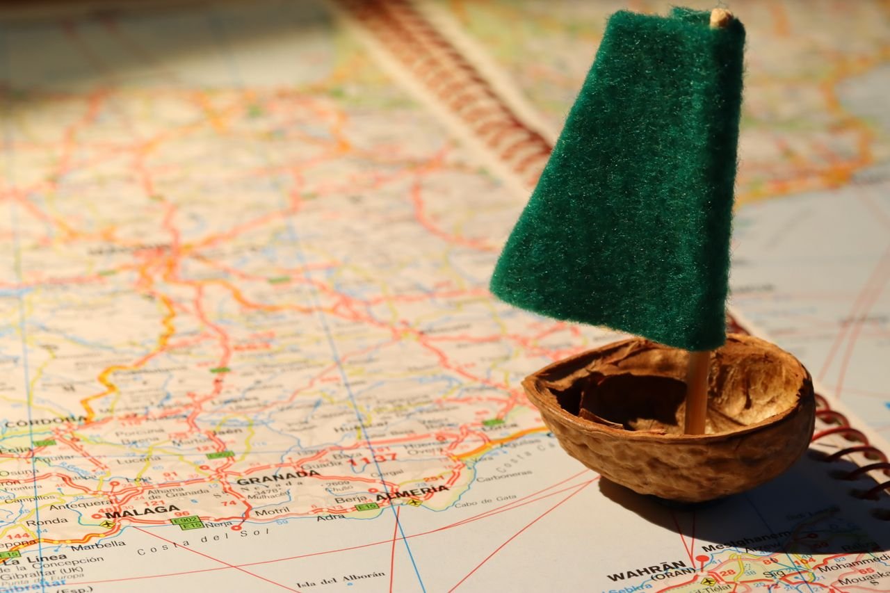 Creative travel metaphor with a tiny sailboat on a detailed world map.